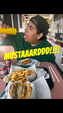 a man in a green hoodie is eating a hamburger and french fries with mustaarddd written in yellow