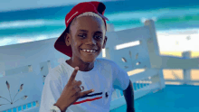 a young boy wearing a red hat and a white shirt is smiling and giving a peace sign