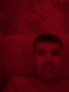 a man without a shirt is taking a selfie in a dark room with a red background .