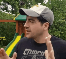 a man wearing a hat and a black shirt with the word sturgis on it is standing in front of a playground .