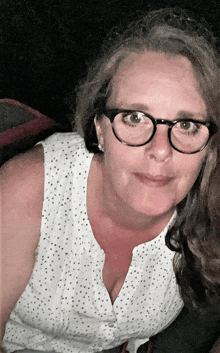 a woman wearing glasses and a white tank top smiles for the camera