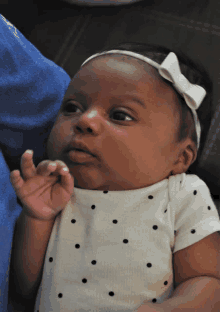 a baby wearing a white polka dot shirt and a white bow on her head