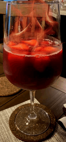 a glass of red liquid with flames coming out of it on a table