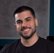 a man with a beard wears a black shirt and smiles for the camera