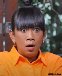 a woman with a surprised look on her face is wearing an orange shirt with the name murulina on it