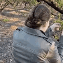 a woman in a leather jacket is sitting under a tree in a park .