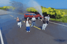 a group of people are dancing on a road in front of a car that has smoke coming out of it