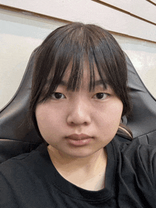 a woman with a black shirt and bangs is sitting in a chair