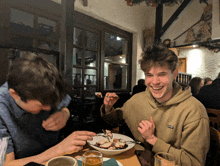 two young men are sitting at a table eating food and one of them is wearing a tan sweatshirt that says yale on the front