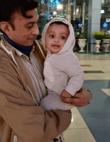 a man is holding a baby in his arms and the baby is wearing a hooded jacket