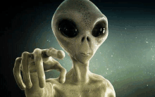 a gray alien is pointing at the camera with his finger .