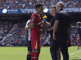 a soccer player shakes hands with a referee on a field with a universal customs clearance banner in the background