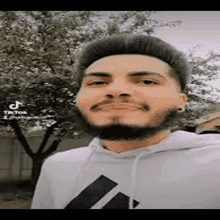 a young man with a beard is wearing a white hoodie and smiling .