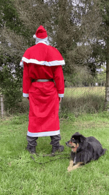 a man dressed as santa claus stands next to a black dog on a leash