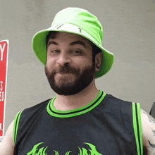 a man wearing a green hat and a black tank top stands in front of a sign that says no parking