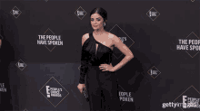 a woman in a black jumpsuit is standing in front of a wall that says " the people have spoken "