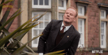 a man in a suit and tie is standing in front of a building with netflix written on the bottom