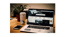 a dell laptop sits on a desk next to a cup of coffee and a cell phone