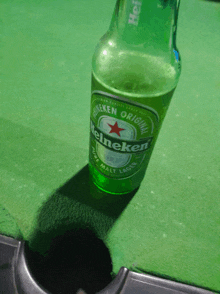 a green bottle of heineken sits on a green surface