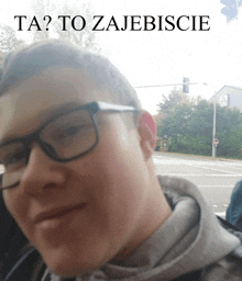 a man wearing glasses is standing in front of a sign that reads ta to zajebiscie