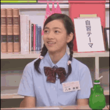 a young girl in a school uniform is sitting at a desk in front of a bookshelf with chinese writing on it .