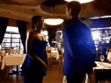 a man and woman are dancing in a restaurant . the woman is wearing a blue dress .