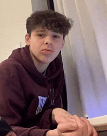 a young man with curly hair wearing a hoodie with the letter t on the front