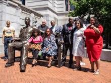 a group of people standing around a statue of a man sitting on a bench