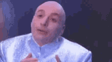 a bald man in a blue suit is making a funny face with his hands .