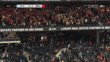 a crowd of people in a stadium watching a game between nyc and rbny with advertisements for partners in abu dhabi