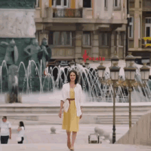 a woman in a yellow dress is walking in front of a fountain with a red arrow pointing to the right