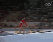 a woman in a red leotard is doing a trick on a trampoline with the olympics logo in the background