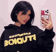 a woman in a black hoodie is taking a picture of herself with her phone .