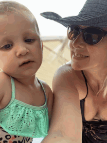 a woman wearing sunglasses and a hat holds a little girl in her arms