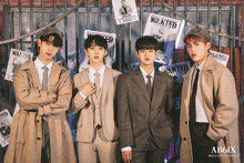 a group of young men are posing in front of a fence with wanted posters on it