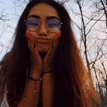 a woman wearing glasses and a bracelet holds her hands to her face