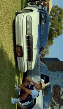 a man sitting in front of a white car with a license plate that says phoenix county