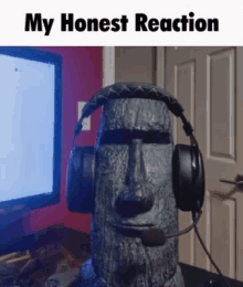 a statue of a moai wearing headphones in front of a computer monitor