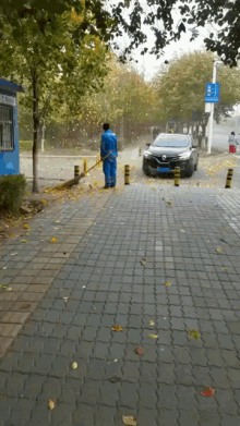 a man is sweeping leaves on the sidewalk in front of a car that has a license plate that says yjc 88