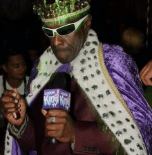 a man wearing a purple cape and a crown is holding a king king tv microphone