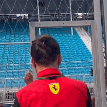 a man in a red jacket with a ferrari logo on it is standing in front of a stadium .