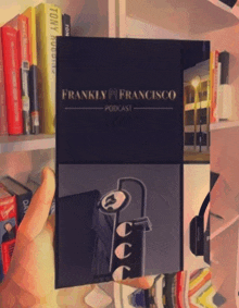 a person is holding a frankly francisco podcast in front of a bookshelf