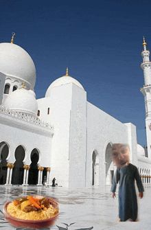 a man in a blue robe stands in front of a white mosque