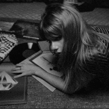 a black and white photo of a girl laying on the floor looking at a record