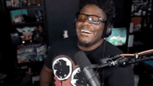 a man wearing headphones and sunglasses is laughing in front of a microphone in a room .