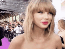 taylor swift is standing on a purple carpet in front of a crowd .