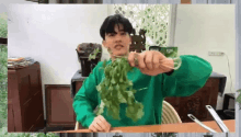 a man in a green sweater is sitting at a table holding a bunch of greenery .