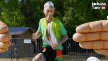 a man in a green jacket is kicking a soccer ball in a park while being surrounded by fingers .