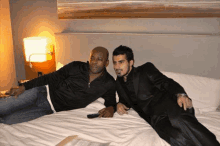 two men are laying on a bed looking at something