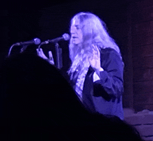 a man with long hair singing into a microphone in a dark room